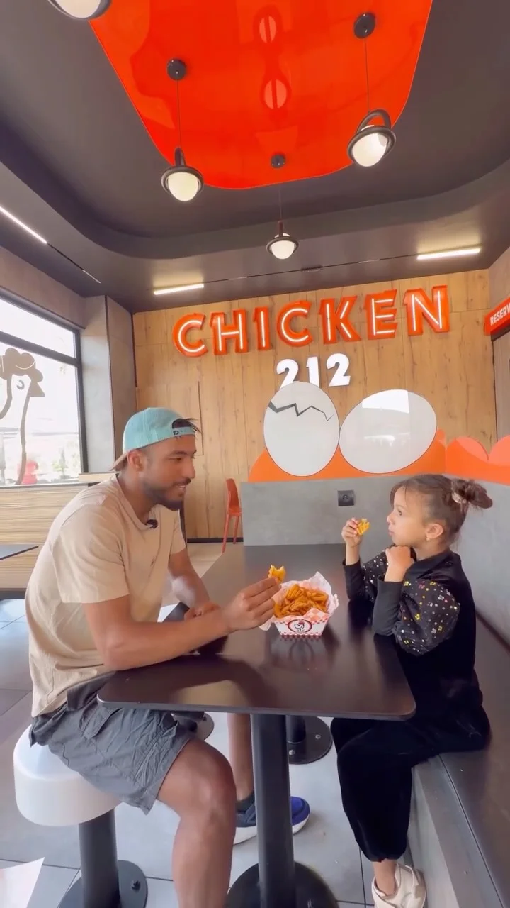 Un adulte et une enfant partagent du poulet à une table chez 212 Chicken